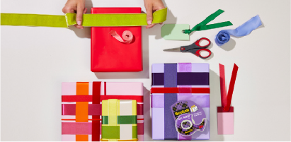 Mãos que envolvem a caixa de presente com o envolvimento original em roxo e vermelho, packshot Fita de presente Scotch®.
