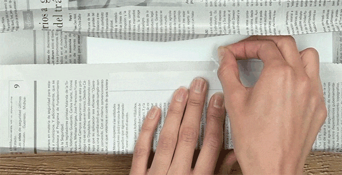 Mãos de mulher dobrando uma folha de jornal.
